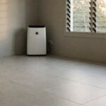 A room with light grey tile flooring, a dehumidifier against the wall, and louvred windows