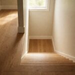 An upstairs hallway with warm oak plank flooring looking down a stairwell to the level below