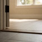 A doorway with a raised timber threshold between a grey tile floor and a wood floor beyond